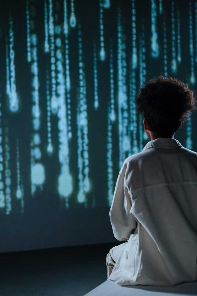 Teenager sitting in front of digital screen with abstract code projection.